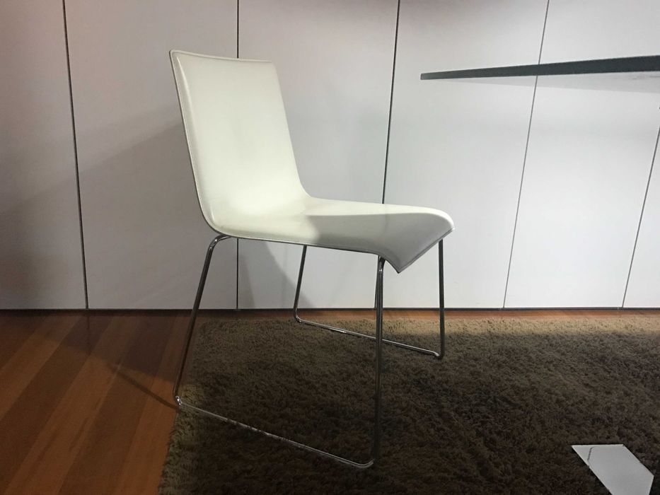 quatro cadeiras de pele branca e base em inox