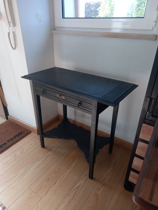 Mesa de apoio preta, antiga. Tem 2 abas pequenas e uma gaveta.