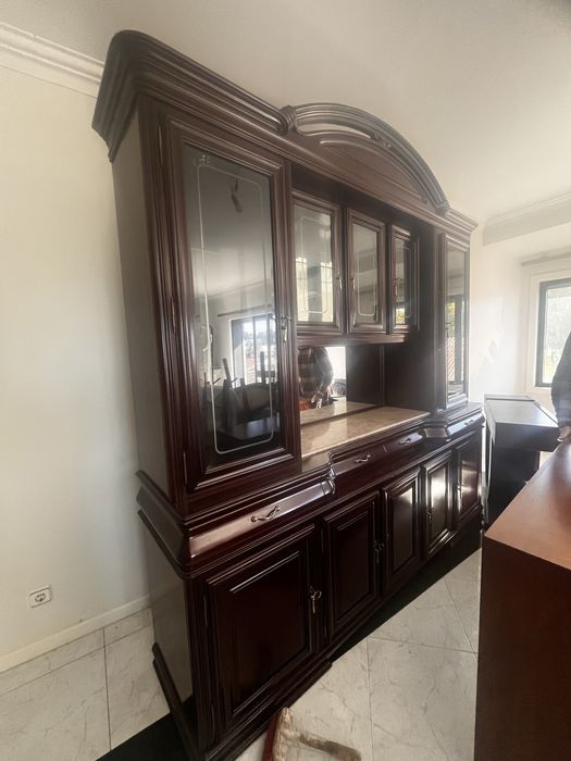 cristaleira/móvel de sala clássico em madeira escura (estilo mogno ou mutene), um tipo de mobiliário robusto e com bastante arrumação.