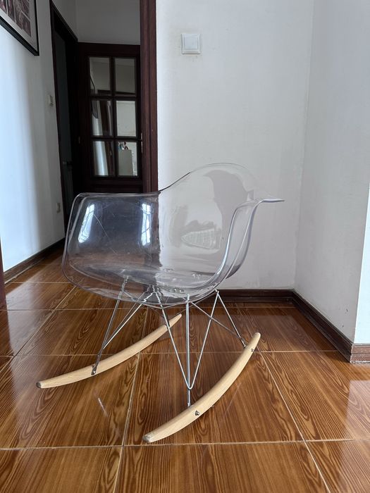 Cadeira de baloiço transparente, que se destaca pelo seu assento translúcido em acrílico combinado com pés de madeira em forma de baloiço
