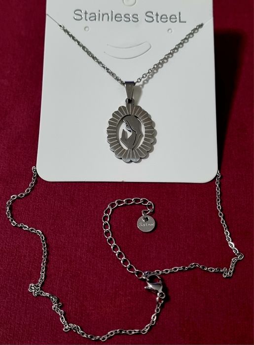 Colar prateado, em aço, com pingente da Nossa Senhora. Tem extensor