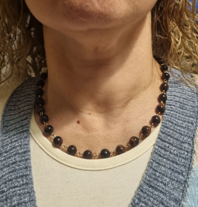 Colar dourado, em aço, às bolinhas castanhas de pedra natural "olho de gato". Tem extensor.