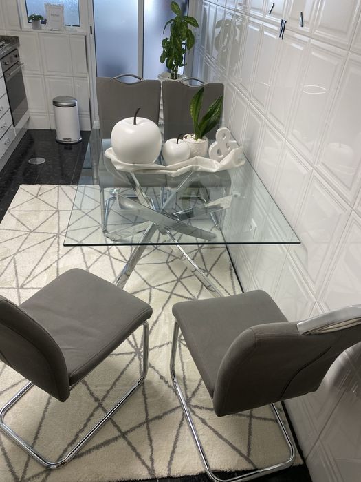 4 cadeiras mais mesa de jantar moderna  com um tampo em vidro transparente e uma elegante estrutura de pernas cruzadas em aço cromado brilhante.
