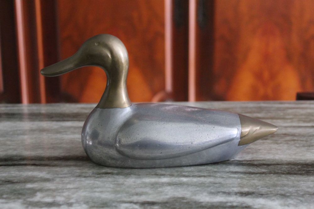 Estatueta vintage de pato, corpo prateado e a cabeça e cauda douradas.