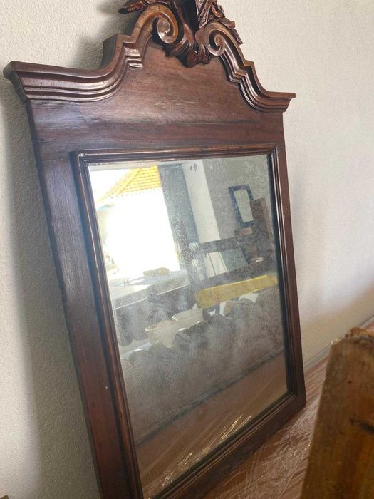 Espelho antigo em mogno, com moldura trabalhada e detalhe decorativo no topo