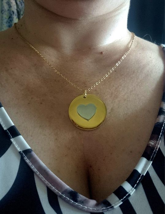 Colar dourado, em aço, com pingente redondo dourado e um coração prateado no centro