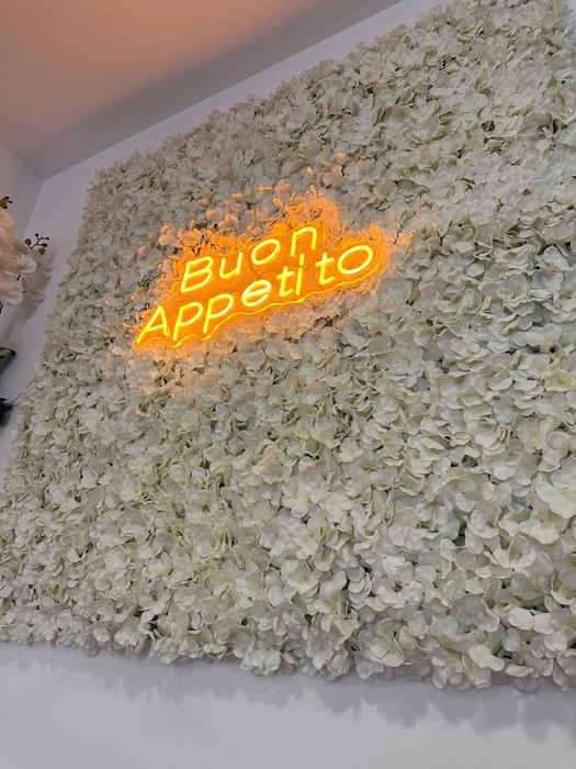 Painel decorativo com flores artificiais e letreiro luminoso “Buon Appetito”