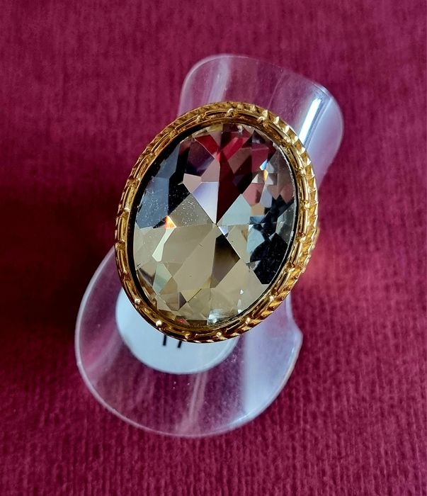 Anel dourado, em aço, com grande pedra de vidro transparente oval. T17
