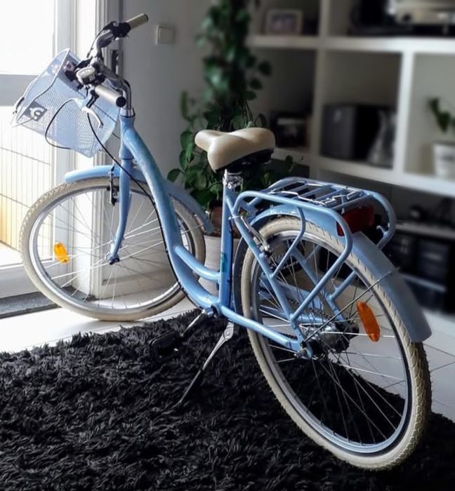 Bicicleta de cidade em azul claro, com cesto frontal e grade traseira. Extremamente elegante e bonita.