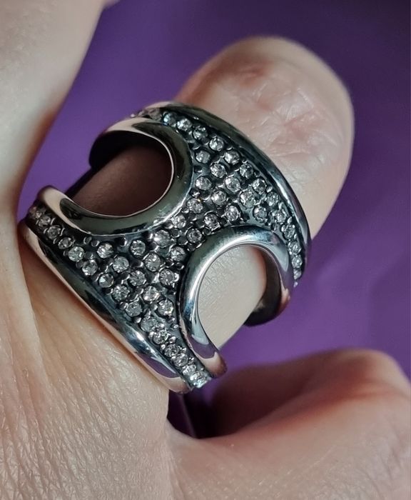 Anel prateado, em aço, aberto dos lados e cheio de zirconias. T17/18