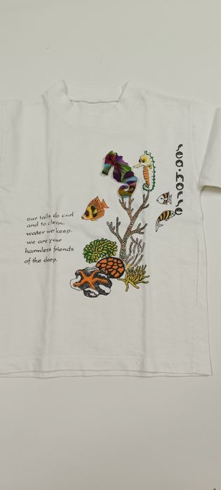 T-shirt branca com bonecos do mar. Tem cavalo marinho a 3D