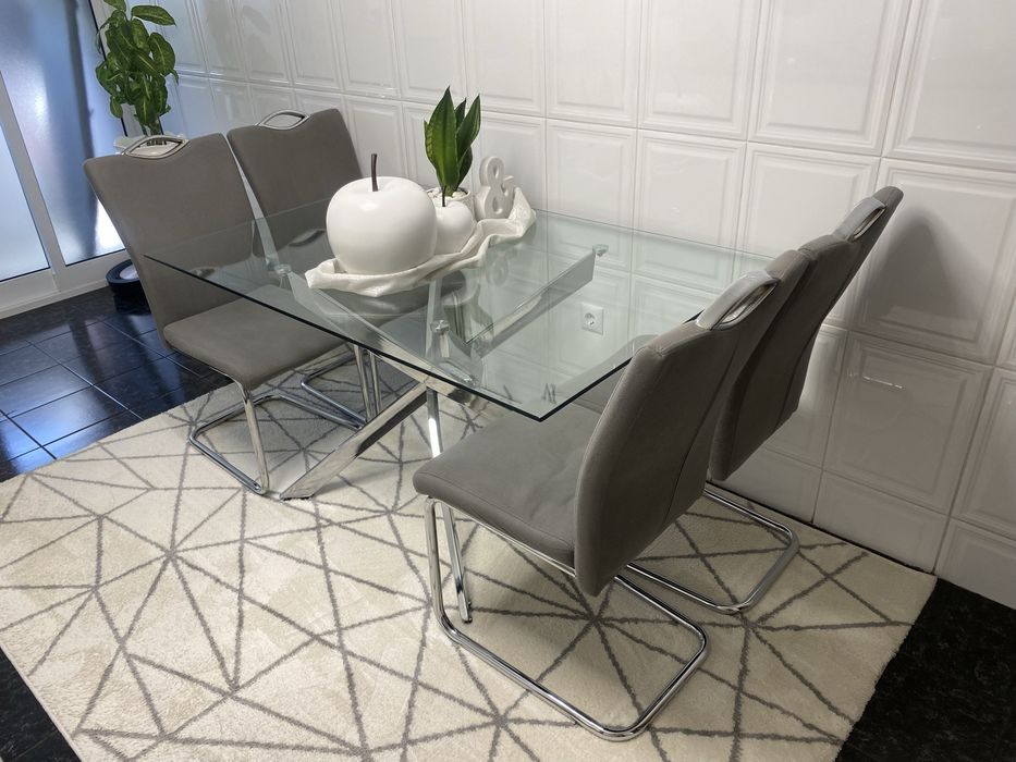 4 cadeiras mais mesa de jantar moderna  com um tampo em vidro transparente e uma elegante estrutura de pernas cruzadas em aço cromado brilhante.