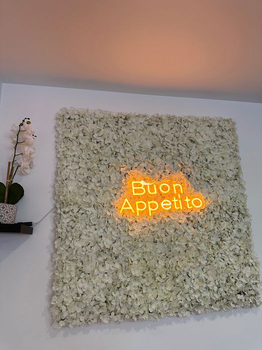 Painel decorativo com flores artificiais e letreiro luminoso “Buon Appetito”