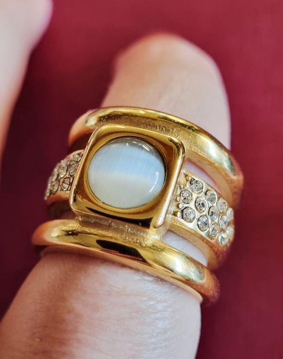 Anel dourado, em aço, com zirconias e uma pedra "olho de gato". T17