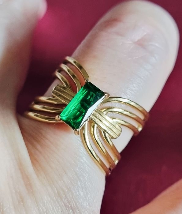 Anel dourado, em aço, com pedrinha retangular verde no centro. Ajustável
