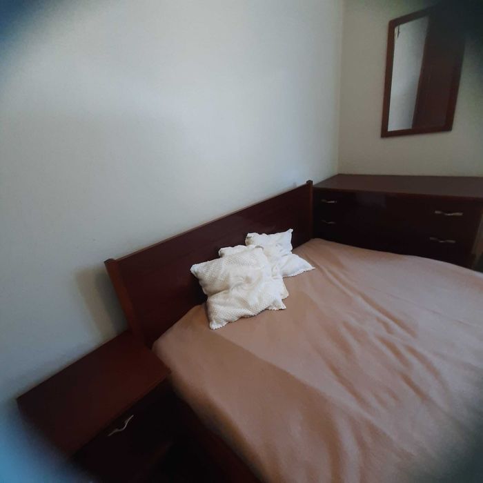 Quarto com cama, mesa de cabeceira, cómoda e espelho