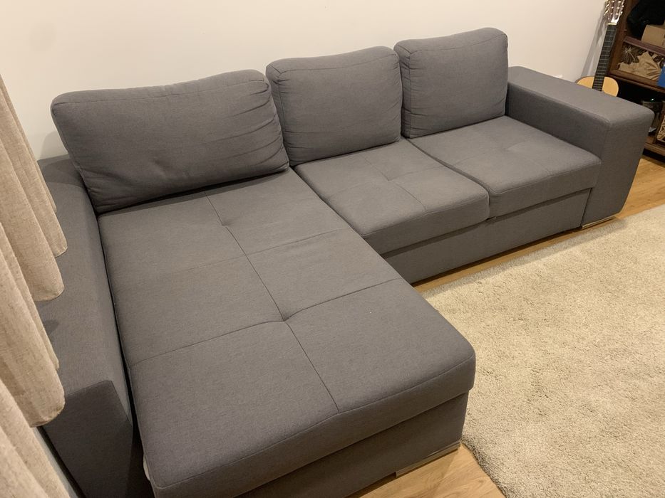 Sofa cama cinza com arrumaçao e dois bancos.