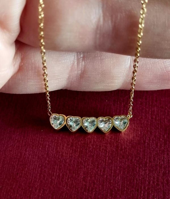 Colar dourado, em aço, com 5 pequenos corações em pedra de vidro.