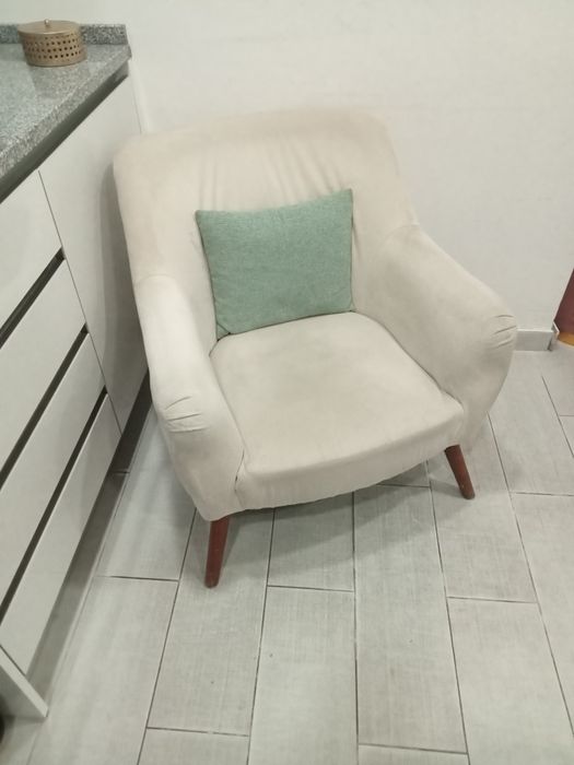 Cadeirão beige com almofada decorativa.