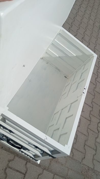 Biała duża skrzynia, kufer z czarnymi okuciami.
