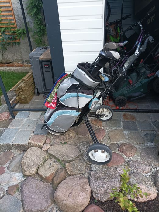 Zestaw kijów golfowych wraz z torbą i wózkiem.