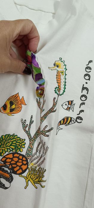 T-shirt branca com bonecos do mar. Tem cavalo marinho a 3D