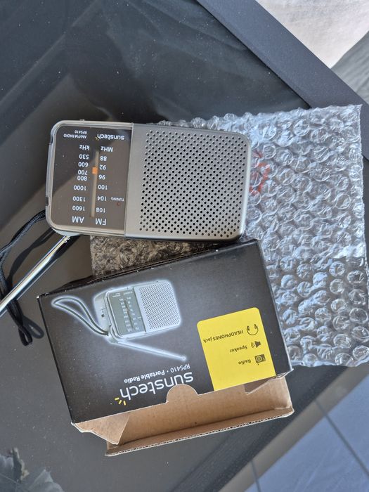 Rádio portátil analógico com tira de fixação e saída para auriculares.
