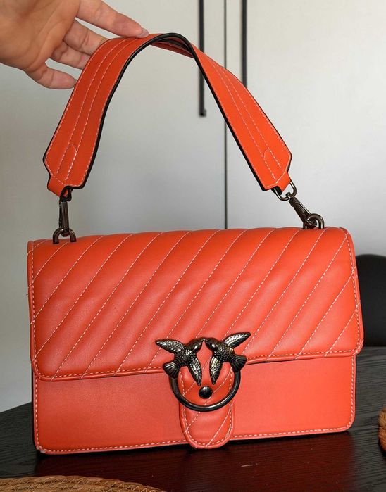 Orange quilted bag with a bird-themed clasp