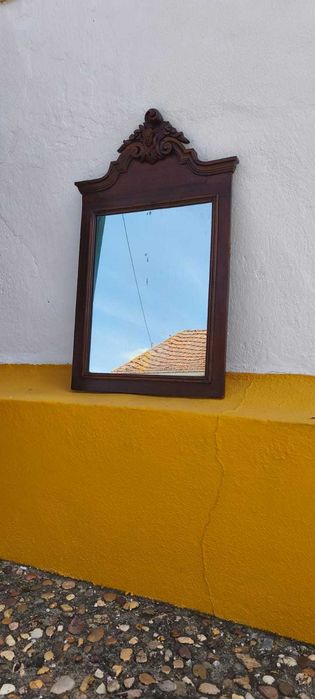 Espelho antigo em mogno, com moldura trabalhada e detalhe decorativo no topo