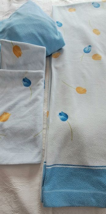 conjunto de cama é composto por um lençol de cima e duas fronhas, todos em tecido polar com um estampado de túlipas azuis e amarelas sobre fundo claro