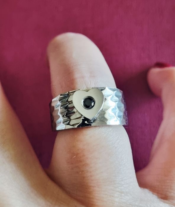 Anel prateado, em aço, com 1 coração com pedrinha preta no centro. T17