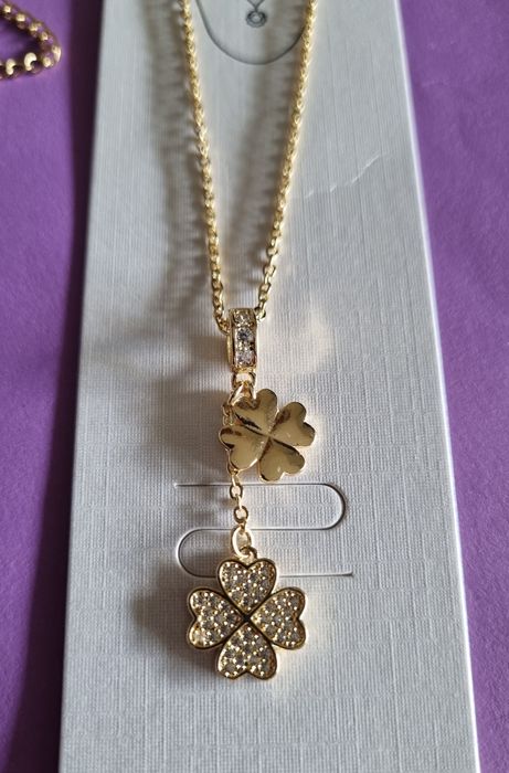 Colar dourado, em aço, com 2 trevos pendentes. Formato gravata.