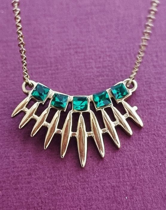 Colar dourado, em aço, com 5 pedrinhas quadradas verdes. Tem extensor.