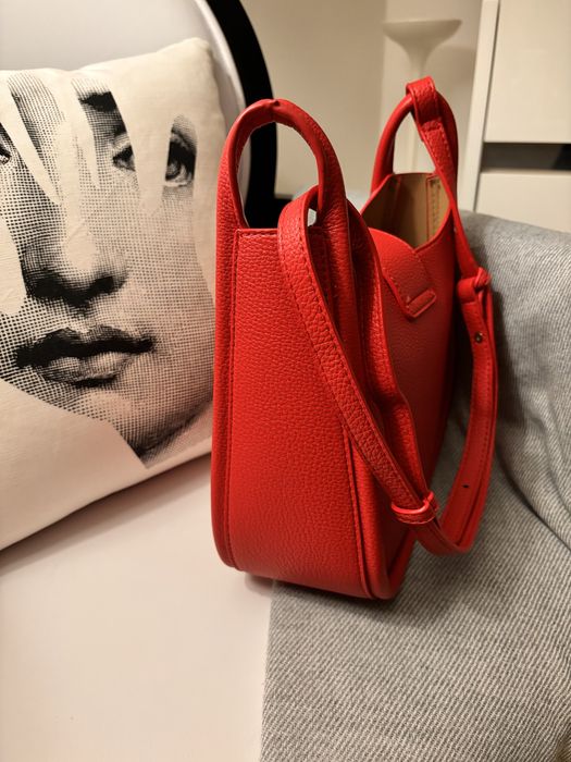 Mala nova, de cor vermelha, com alça à tiracolo.