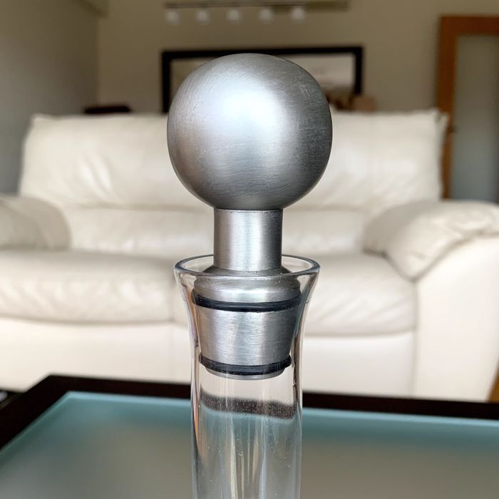 Licoreira de vidro com pormenor decorativo e rolha metálicos.