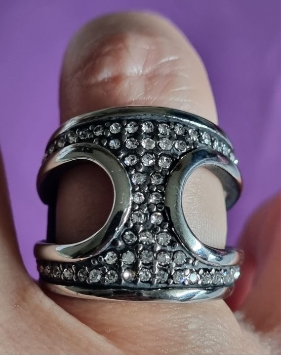 Anel prateado, em aço, aberto dos lados e cheio de zirconias. T17/18