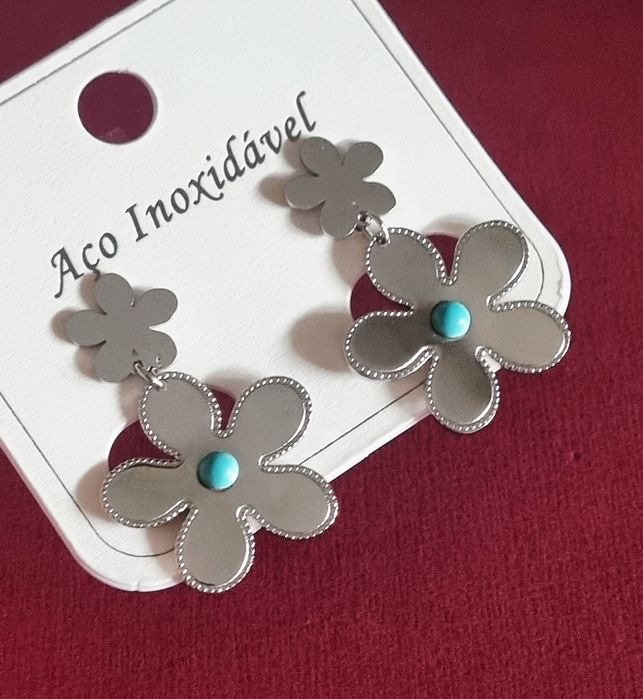 Brincos prateados, em aço, 2 flores de diferentes tamanhos com 1 pedrinha turquesa.