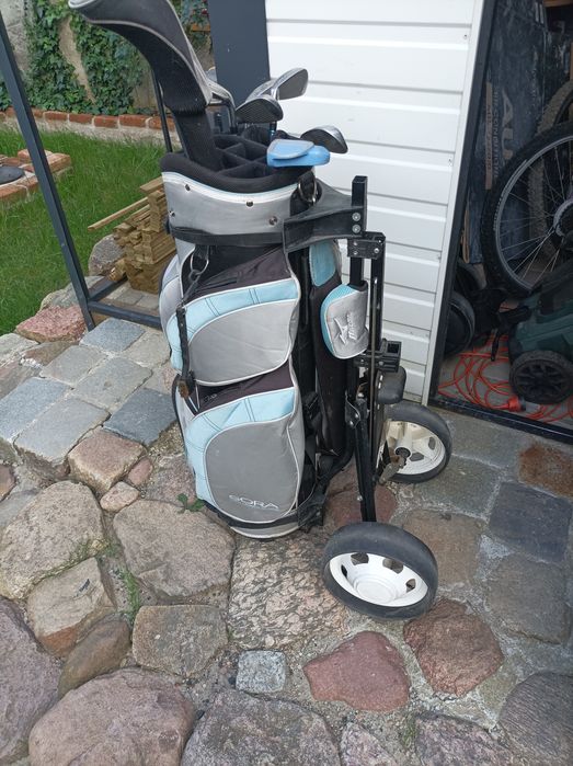 Zestaw kijów golfowych wraz z torbą i wózkiem.