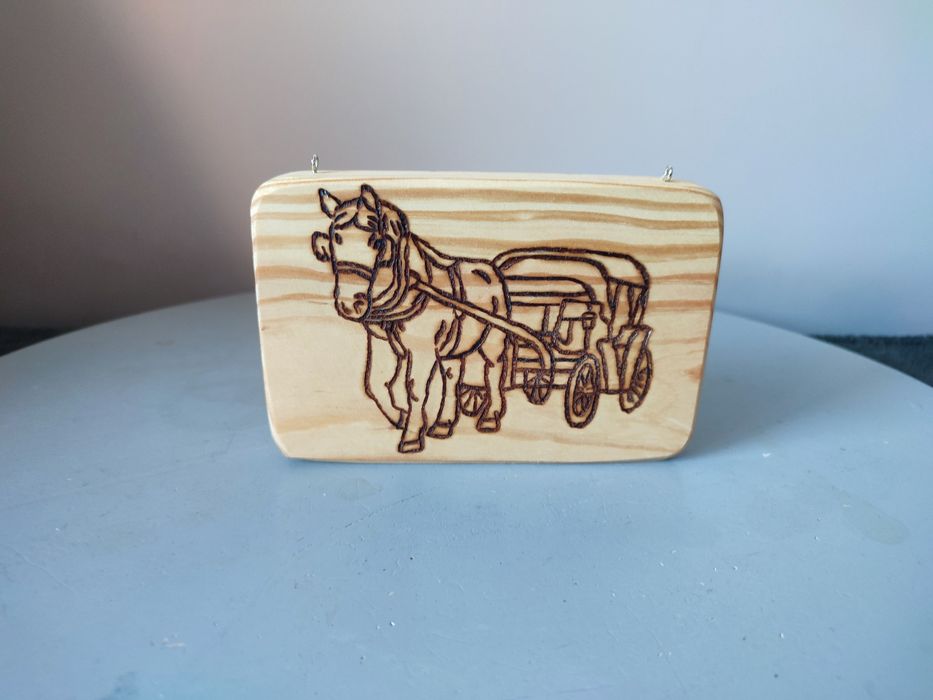 Drewniana tabliczka zawieszana z obrazem konia ciągnącego bryczkę.