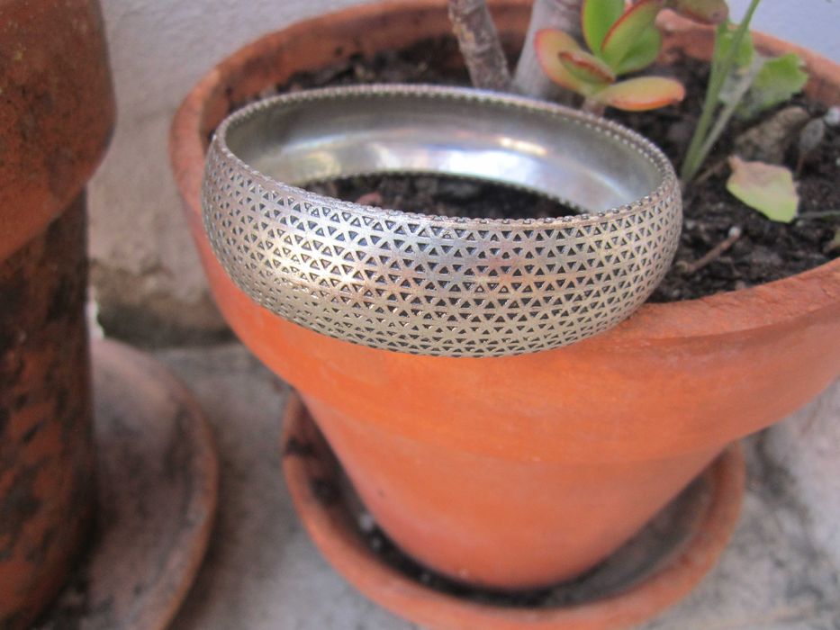 Pulseira rígida prateada com intrincado padrão geométrico triangular perfurado