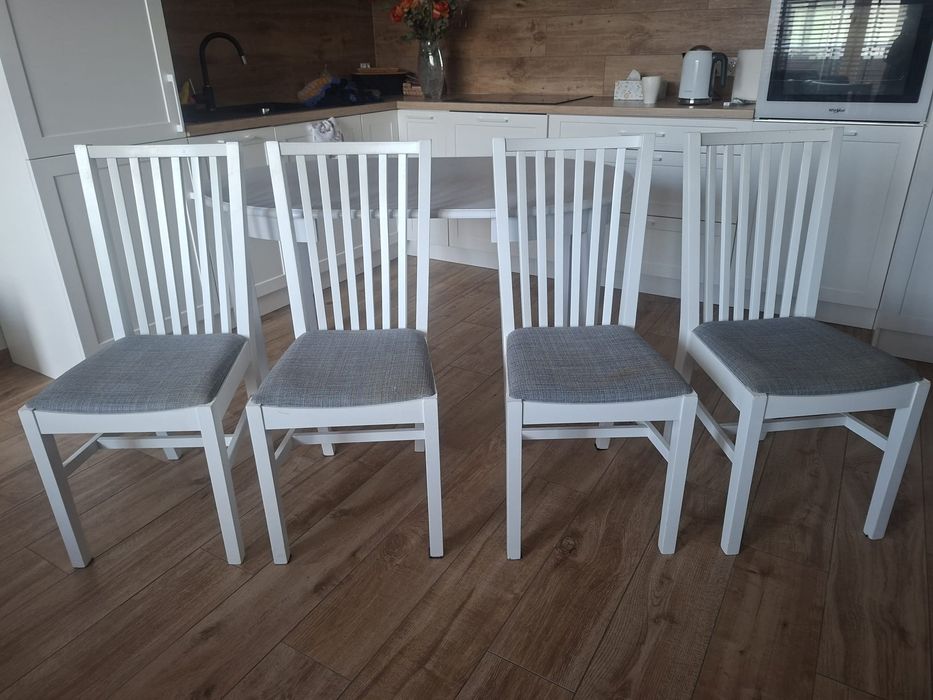 Cztery białe krzesła z tapicerowanymi siedziskiem