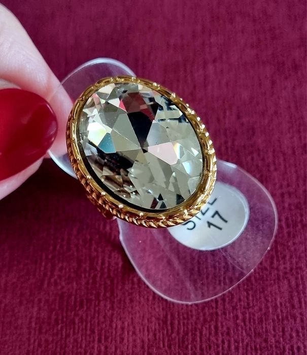 Anel dourado, em aço, com grande pedra de vidro transparente oval. T17