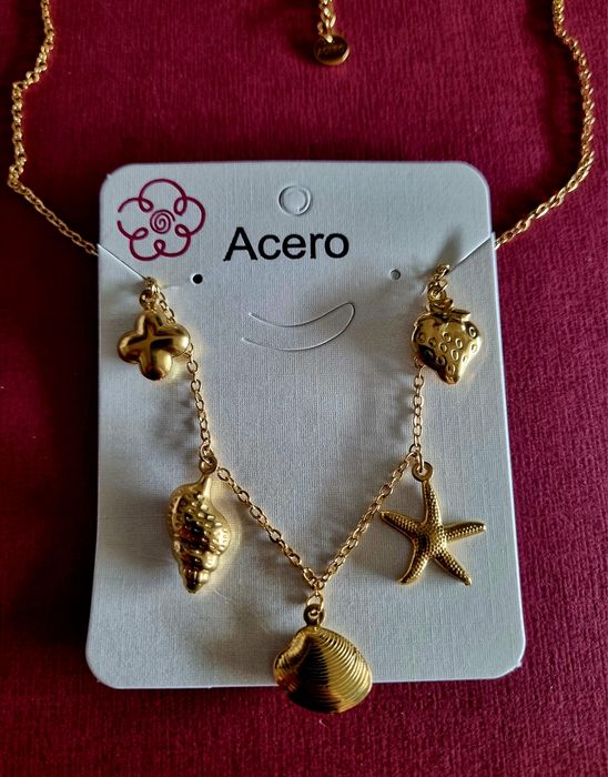 Colar dourado, em aço, com 5 pingentes diferentes. Tem extensor.
