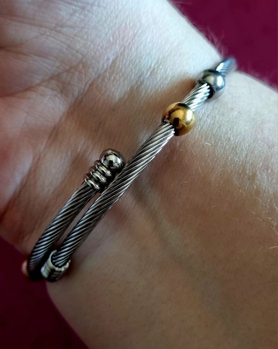 Pulseira prateada, em aço, com bolinhas douradas e um trevo da sorte.