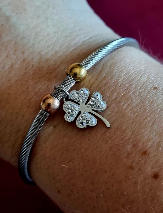 Pulseira prateada, em aço, com bolinhas douradas e um trevo da sorte.