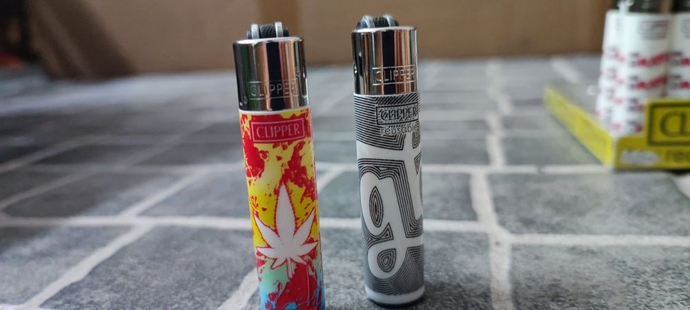 Conjunto de dois  Clipper Mini colecionáveis. Cada um tem um design único e vibrante.

- Um com padrão de folha  em vermelho e amarelo.
- Um com padrã