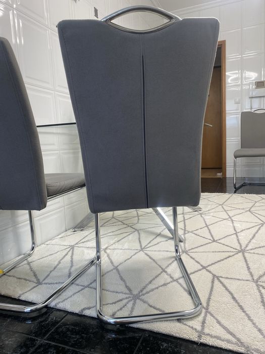4 cadeiras mais mesa de jantar moderna  com um tampo em vidro transparente e uma elegante estrutura de pernas cruzadas em aço cromado brilhante.