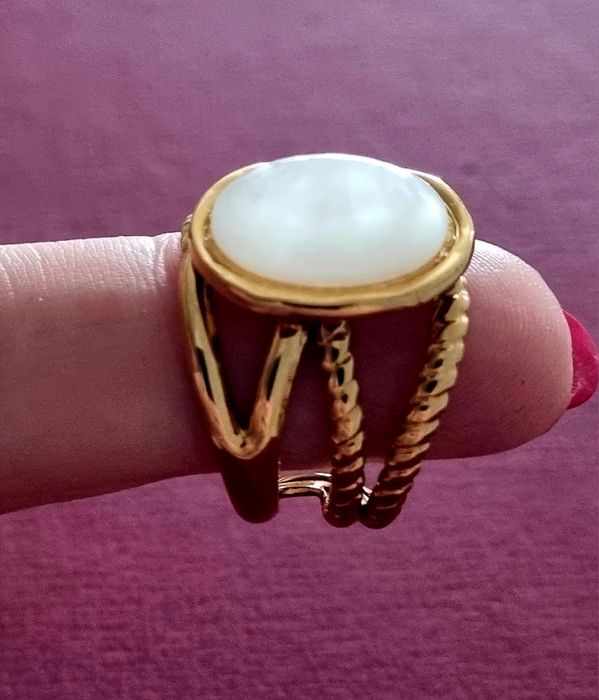 Anel dourado, em aço, com uma  madrepérola  oval no centro. Ajustável
