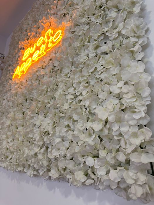 Painel decorativo com flores artificiais e letreiro luminoso “Buon Appetito”