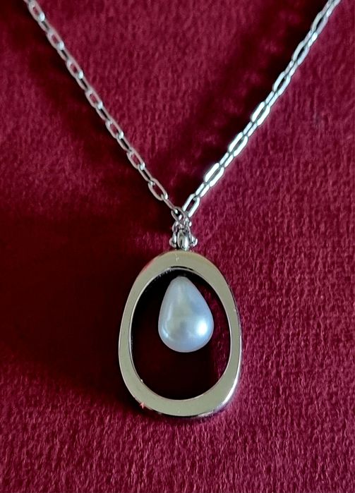 Colar prateado, em aço, com pingente oval e 1 pérola no centro. Tem extensor